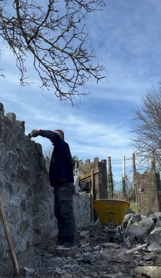 A stone wall being built up course by course against an open sky